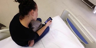 美丽的女病人在医院病床上使用智能手机。手术后等待出院
