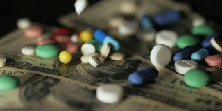 药丸落在钞票上，昂贵的药品，制药生意。药店的主题。多色药片和胶囊的钞票。慢动作