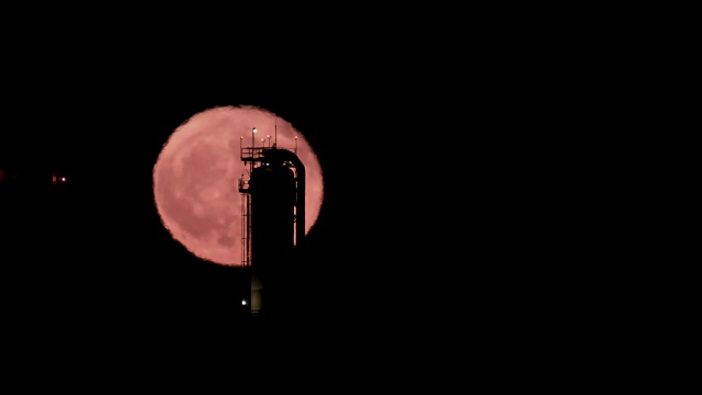 红色的满月从大型炼油厂后面升起