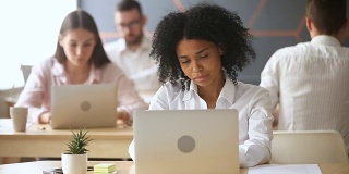 无聊的非洲裔美国女商人在同事的工作场所用笔记本电脑接听电话