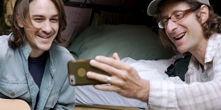 两个英俊的男人谈论自拍与他们的智能手机露营在一起