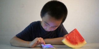 亚洲男孩坐在桌子前，高兴地吃着西瓜
