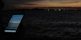 日落时分，年轻女性在热带海滩上使用手机。晚上在海滩上拿着智能手机的女孩。