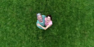 一对成熟的夫妇站在绿色的草坪上，对着镜头微笑着挥手