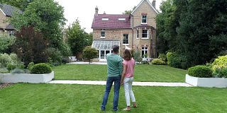 成熟的夫妇站在后花园，欣赏他们的家与建筑俯视图