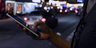 近距离观察女人的手，在她的智能手机上写信息与汽车灯光背景。