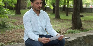 悲伤的男人在公园里，读着，撕着一个字母。