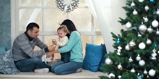 美丽的圣诞节快乐的家庭和小女孩坐在窗台上编织毛衣