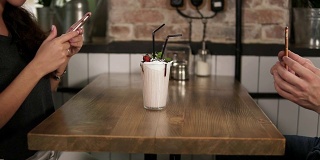 男男女女在用手机拍一杯奶昔，上面放着樱桃，在咖啡馆的木桌上放着稻草