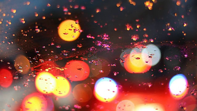 在雨天的天气下开车行驶在城市街道上，雨点落在挡风玻璃上带着模糊的灯光的车辆行驶在交通堵塞的城市道路上