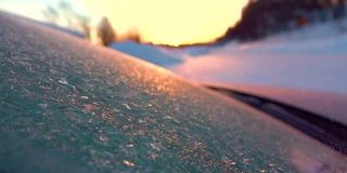 用手刮掉结冰的汽车挡风玻璃上的霜，雪花在阳光下飘动