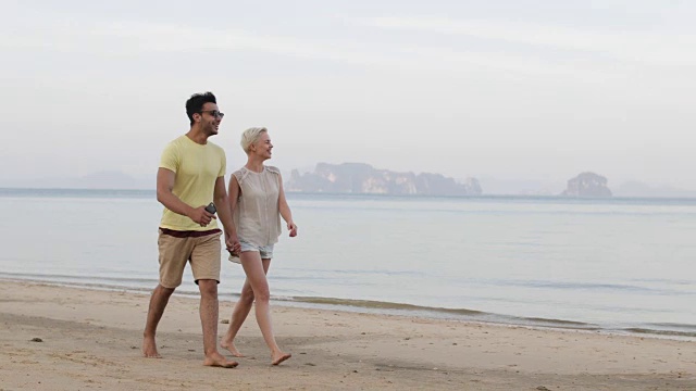 一对情侣在海滩上牵着手聊天，西班牙男人和年轻女人指指点点，游客度假