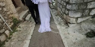 新婚夫妇的新娘和新郎只看背影走在狭窄的街道上，古老的意大利或法国城镇慢镜头。年轻的妻子穿着白色的带花边的婚纱。欧洲旅游婚礼