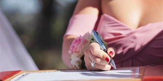 女子在婚礼上签署结婚登记证文件的特写慢镜头。女手握笔，男手指指签婚前协议的位置