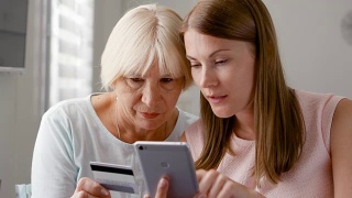 年长的母亲和她的小女儿在家里使用智能手机。用手机刷卡购物视频素材模板下载