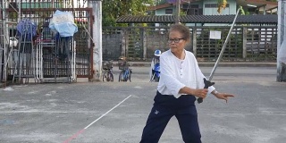 一位老妇人在停车场练习中国剑舞