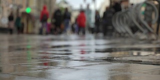 雨后的城市街道。一群人走在潮湿光亮的人行道上。水坑里映出人影的影子。秋天的概念在夏日的雨中模糊。城市街道上的雨天背景。真正的时间。人们在雨中打着伞去