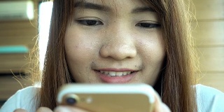 一名女子在咖啡馆用智能手机上的应用程序边喝咖啡边笑边发短信。美丽的多元文化年轻随意女性专业手机。混血亚裔白种人模型。