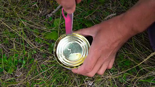 强壮的男子用手打开一个铁罐，用刀在草地上切鱼，在上面拍摄特写镜头。