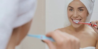 一个头裹毛巾的漂亮女人在浴室的镜子前刷牙