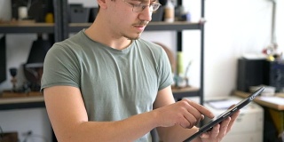年轻的男性手工艺人在他的工作室里工作，在平板电脑上搜索。