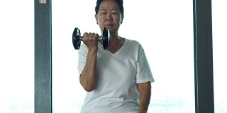 亚洲资深女子举着哑铃，在健身室进行健康锻炼