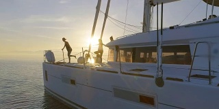 航拍三个美丽的健康妇女在一艘白色帆船上做晨瑜伽。平静的大海与升起的太阳和平静的大海。