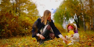 秋天里，当黄色的树叶围着妈妈和小女孩玩着枫叶，笑着，笑着。妈妈在秋天拥抱我的女儿，和她一起玩耍。散景和阳光