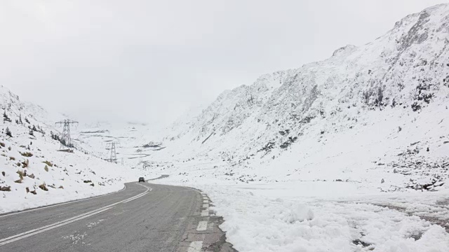 一辆黑色轿车在雪山之间的发夹弯道上行驶