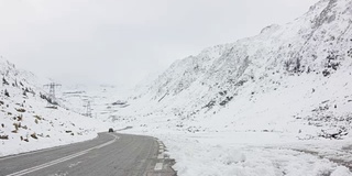 一辆黑色轿车在雪山之间的发夹弯道上行驶