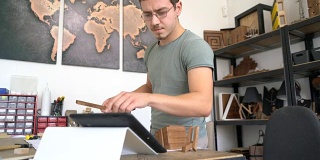 男性手工艺人组装木制项目和检查他的平板电脑。