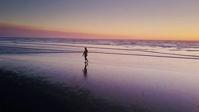 日落时分独自在海滩上行走的女人-无人机拍摄