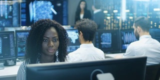 女性计算机工程师与她的多民族专家团队一起从事神经网络/人工智能项目。办公室有多个屏幕显示3D可视化。
