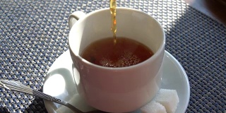 用慢镜头把茶倒进杯子里。咖啡馆室内。阳光照射的表