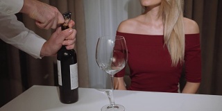 waiter opens a bottle of red wine for a woman in a restaurant