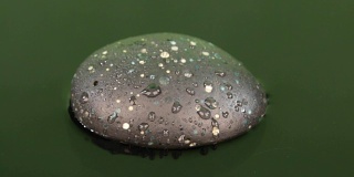 一滴水滴落在绿色水中的一块黑色石头上