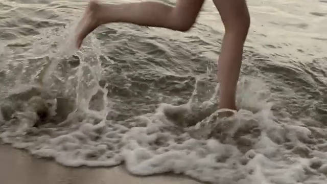 年轻女子的双腿在黎明时穿过大海