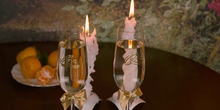 一对新婚夫妇互相碰杯。桌子上燃烧的蜡烛。男性和女性举起一杯葡萄酒和香槟。结婚标志戒指画在眼镜上。