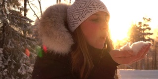 慢镜头:在神奇的冬天，年轻女子在夕阳下吹着雪花