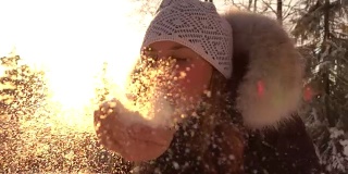 慢镜头:一个年轻女子在神奇的冬日夕阳下吹着闪闪发光的雪花