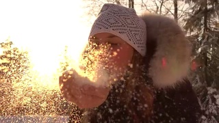 慢镜头:一个年轻女子在神奇的冬日夕阳下吹着闪闪发光的雪花视频素材模板下载