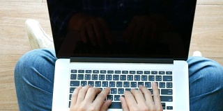 4 k。顶视图的人用他的笔记本电脑，打字，冲浪。男人坐在地板上用笔记本电脑在家里。黑屏笔记本电脑。滑动运动