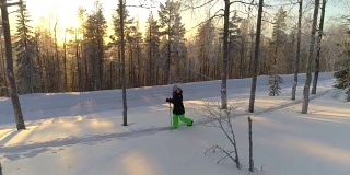 在金色的冬日夕阳下，女孩穿着雪鞋在厚厚的雪地上徒步行走