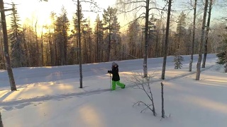 在金色的冬日夕阳下，女孩穿着雪鞋在厚厚的雪地上徒步行走视频素材模板下载