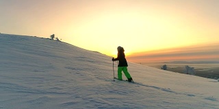 天线:在冬日的夕阳下，活跃的女性穿着雪鞋在白雪覆盖的山坡上徒步