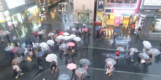 日本大阪道顿堀大街上，一群打着伞的人在下雨