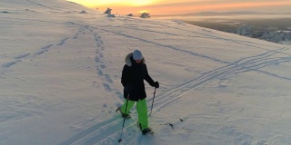 AERIAL:活泼的年轻女子在夕阳下穿着雪鞋走下雪坡