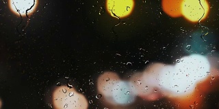 雨点落在车窗上，街道交通灯的背景模糊不清