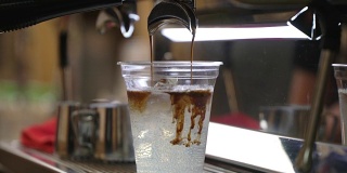 特写新鲜冰咖啡，冷咖啡与冰块在一次性透明杯简单地倒在冰。意大利浓缩咖啡机。咖啡文化和专业的咖啡制作、咖啡送走、服务、餐饮理念