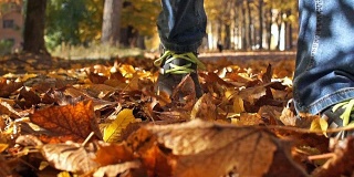在一个阳光明媚的日子里，一个穿着运动鞋和牛仔裤的男人正走在落叶上。
